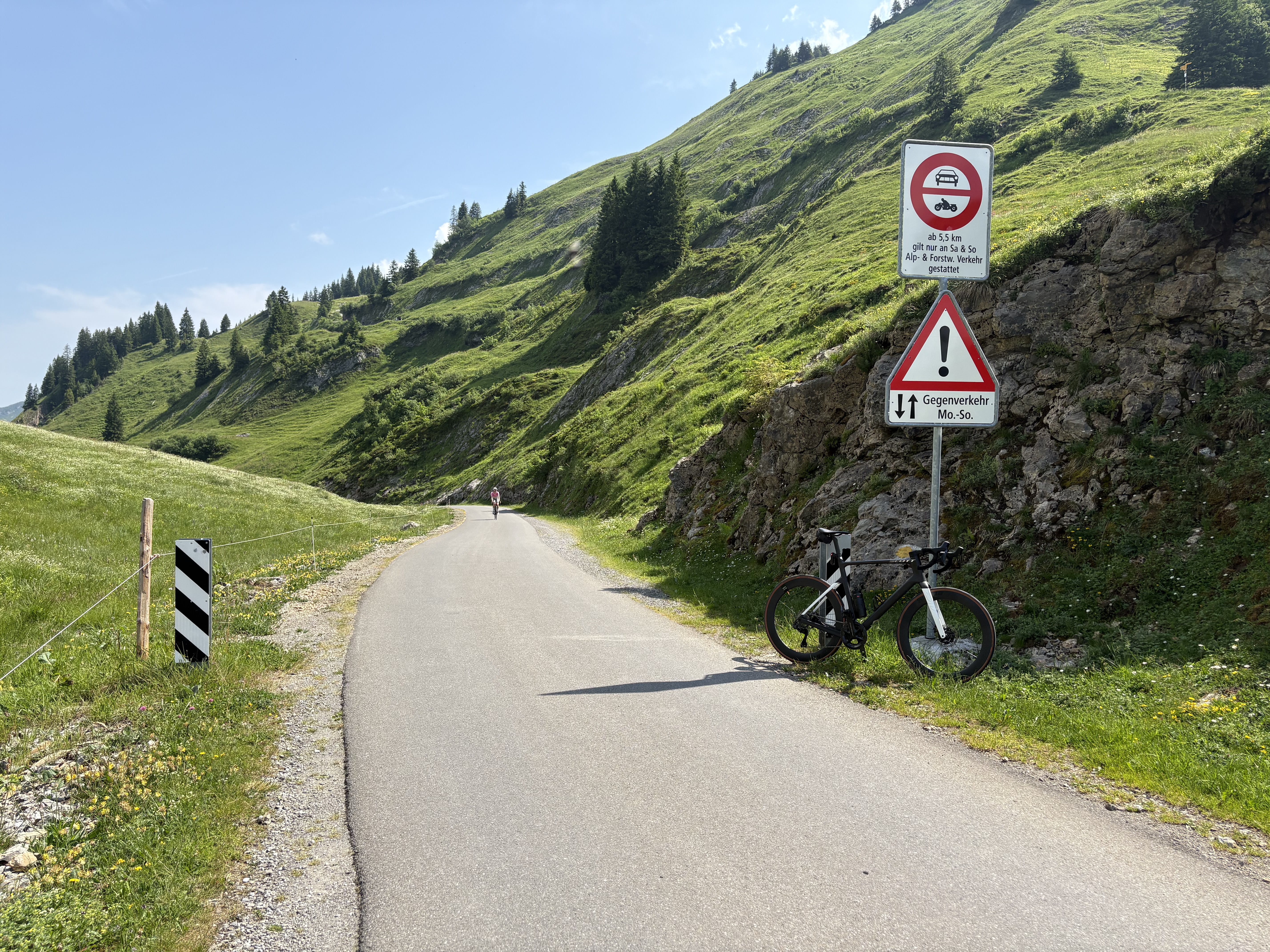 The upper Pragelpass road climbing through alpine pasture, with the pass's traffic-restriction signs marking the road that closes to cars at weekends